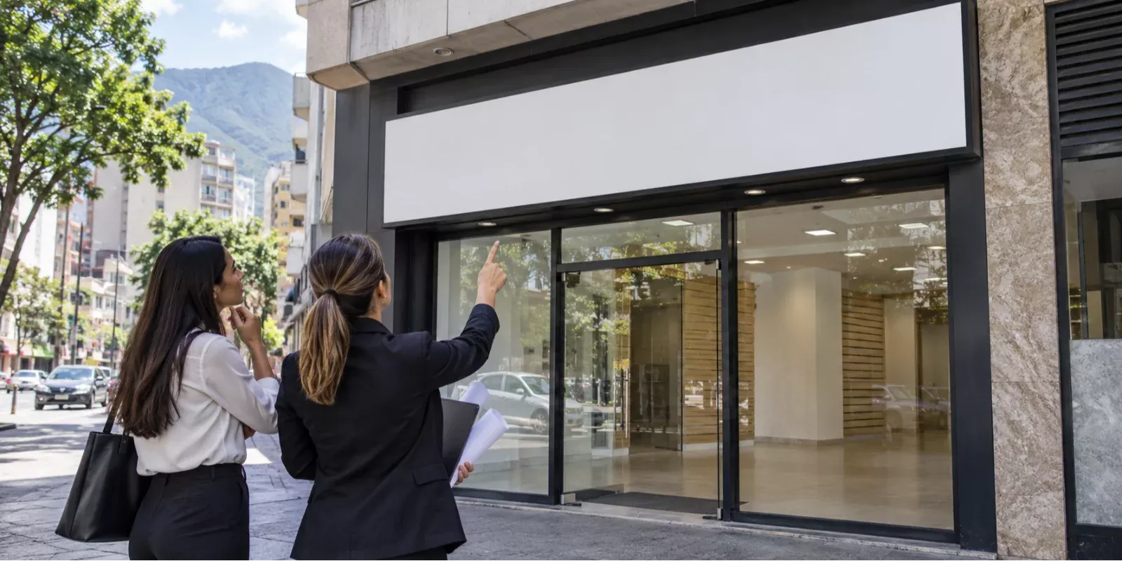 Propietaria y profesional evaluando una fachada con un panel vacío para un posible aviso comercial.
